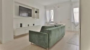 A modern living room with a green sofa, a flat-screen TV, a white console, and a large window with sheer curtains. - Elegant 2-bed apt in the Centre of Milan (Milan)