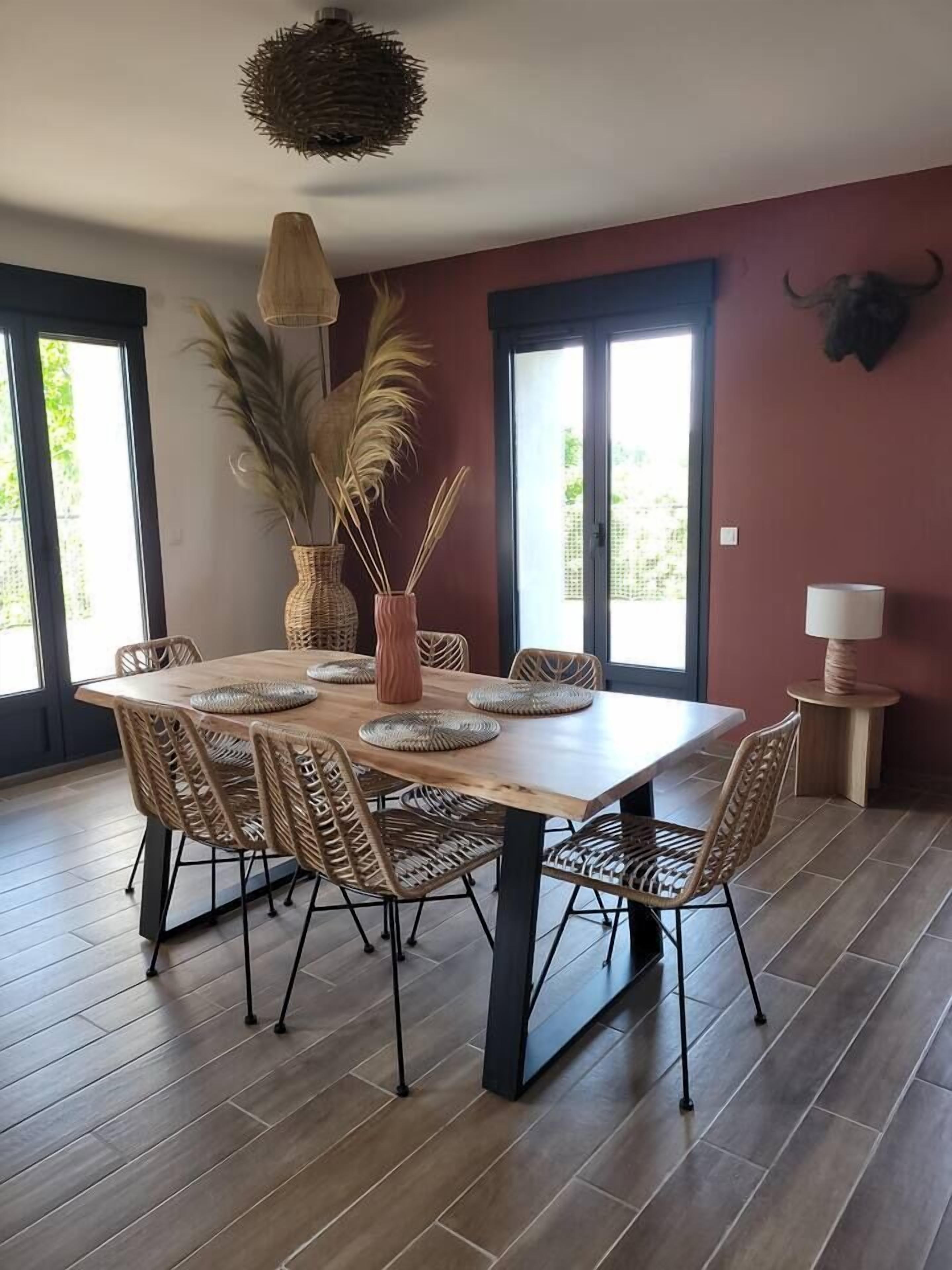 A dining area with a wooden table, wicker chairs, a vase with pampas grass, and a bull's head decoration on the wall.