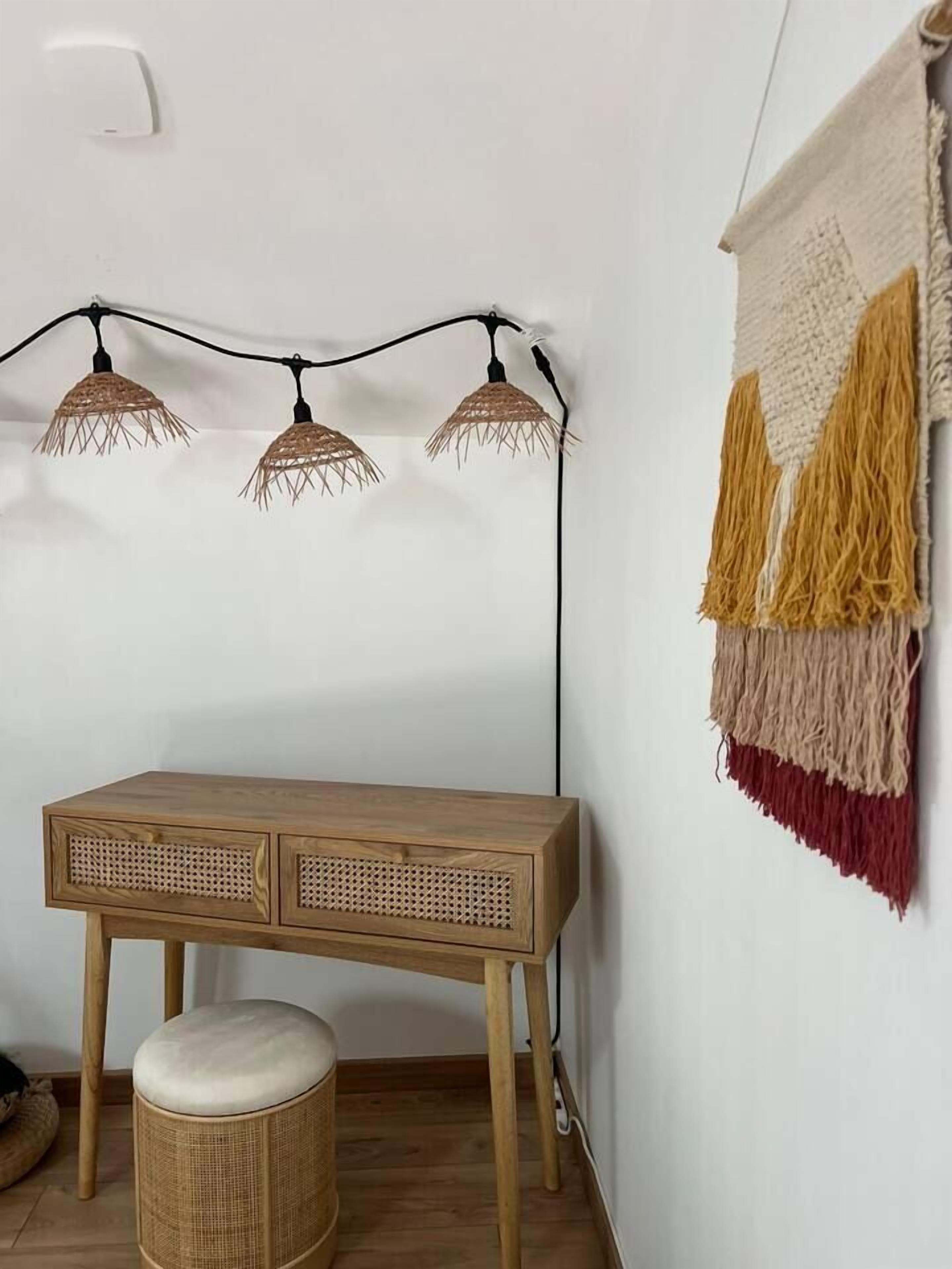 Een kamer met een houten bureau, een geweven kruk en een macramé wanddecoratie.
