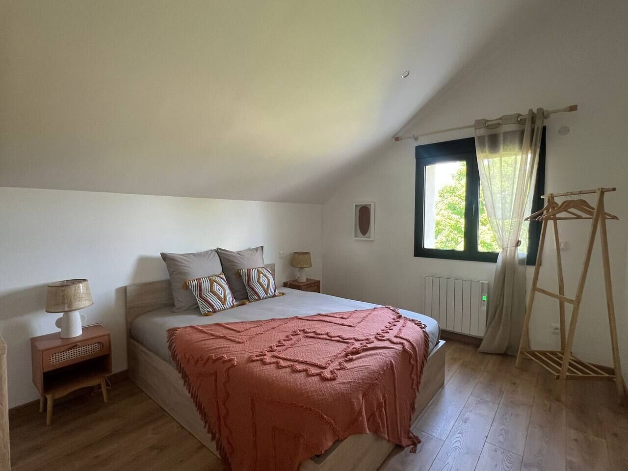 Un dormitorio con cama, mesita de noche, ventana con cortinas y una escalera de madera.