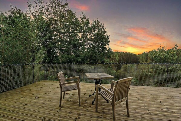 An outdoor deck with a table and chairs, surrounded by a wire fence and trees.