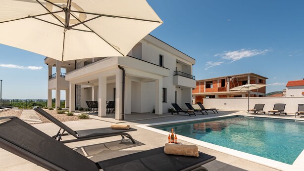 A poolside area with lounge chairs, a large umbrella, and a pool.