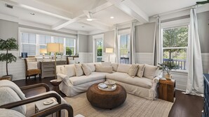 A spacious living room with a sectional sofa, a round wicker coffee table, and a dining area with a table and chairs. - Surf Sanctuary + Golf Cart, Pet Friendly & Bikes (Santa Rosa Beach)