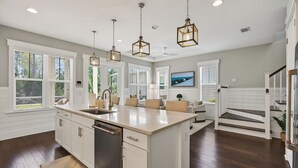 A modern kitchen with a large island, pendant lights, and a view of the outdoors. - Surf Sanctuary + Golf Cart, Pet Friendly & Bikes (Santa Rosa Beach)