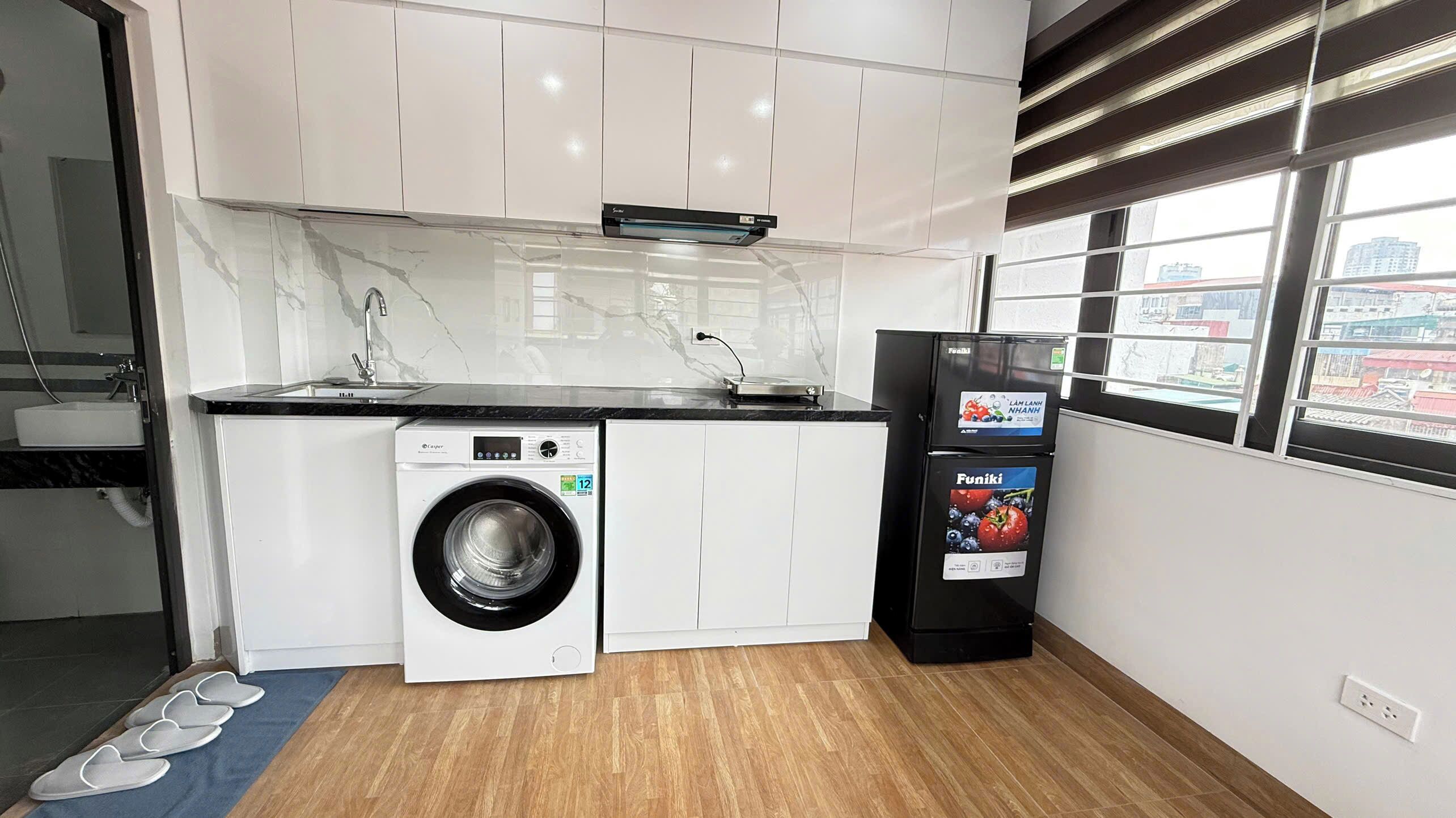 Cocina compacta con lavadora, refrigerador y ventana con vistas a edificios.