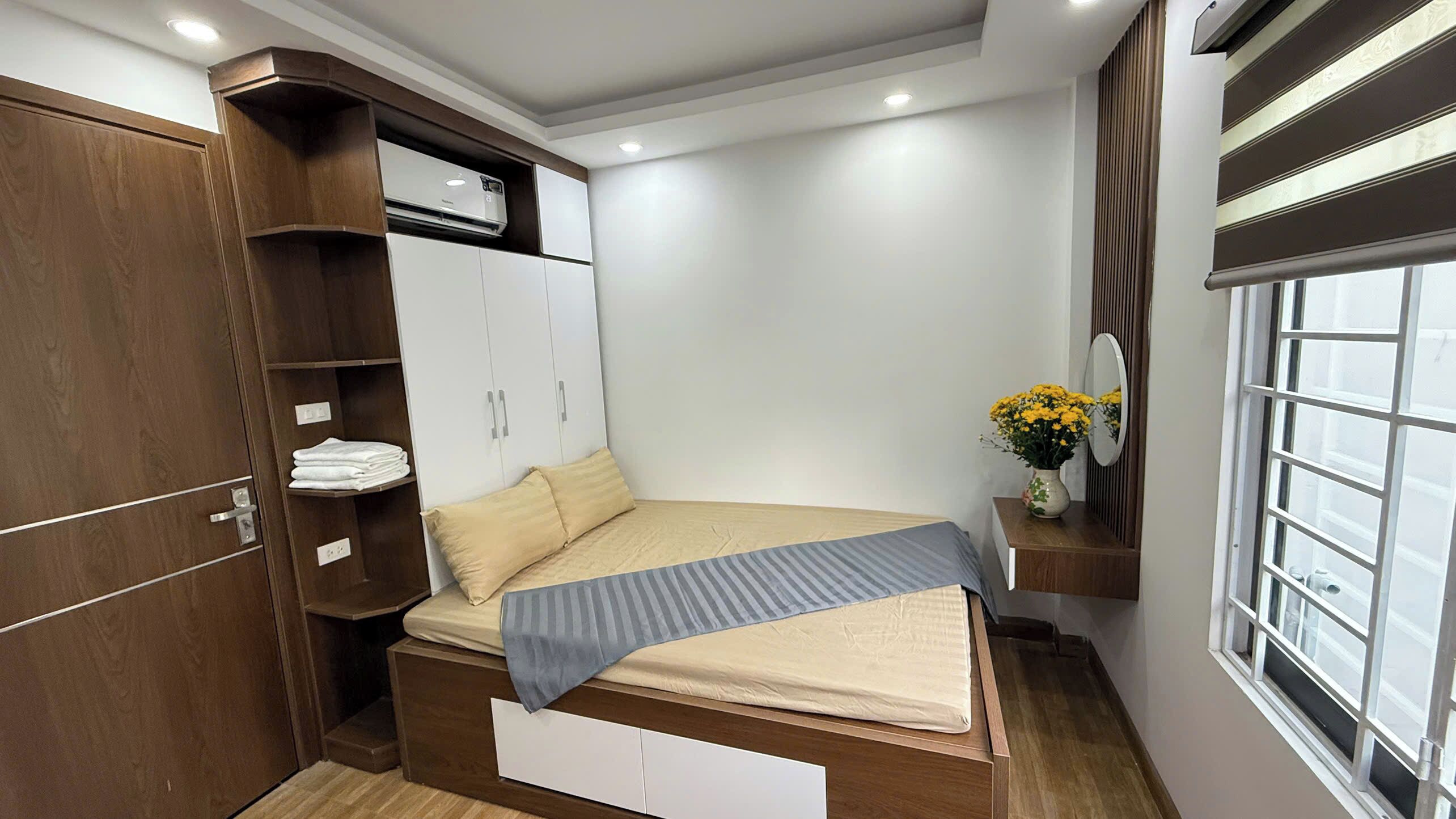 A compact bedroom with a bed, a wardrobe, a vanity with a mirror, and a window.