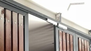 Puerta de metal con listones verticales de madera, techo blanco y señal de salida de emergencia roja.