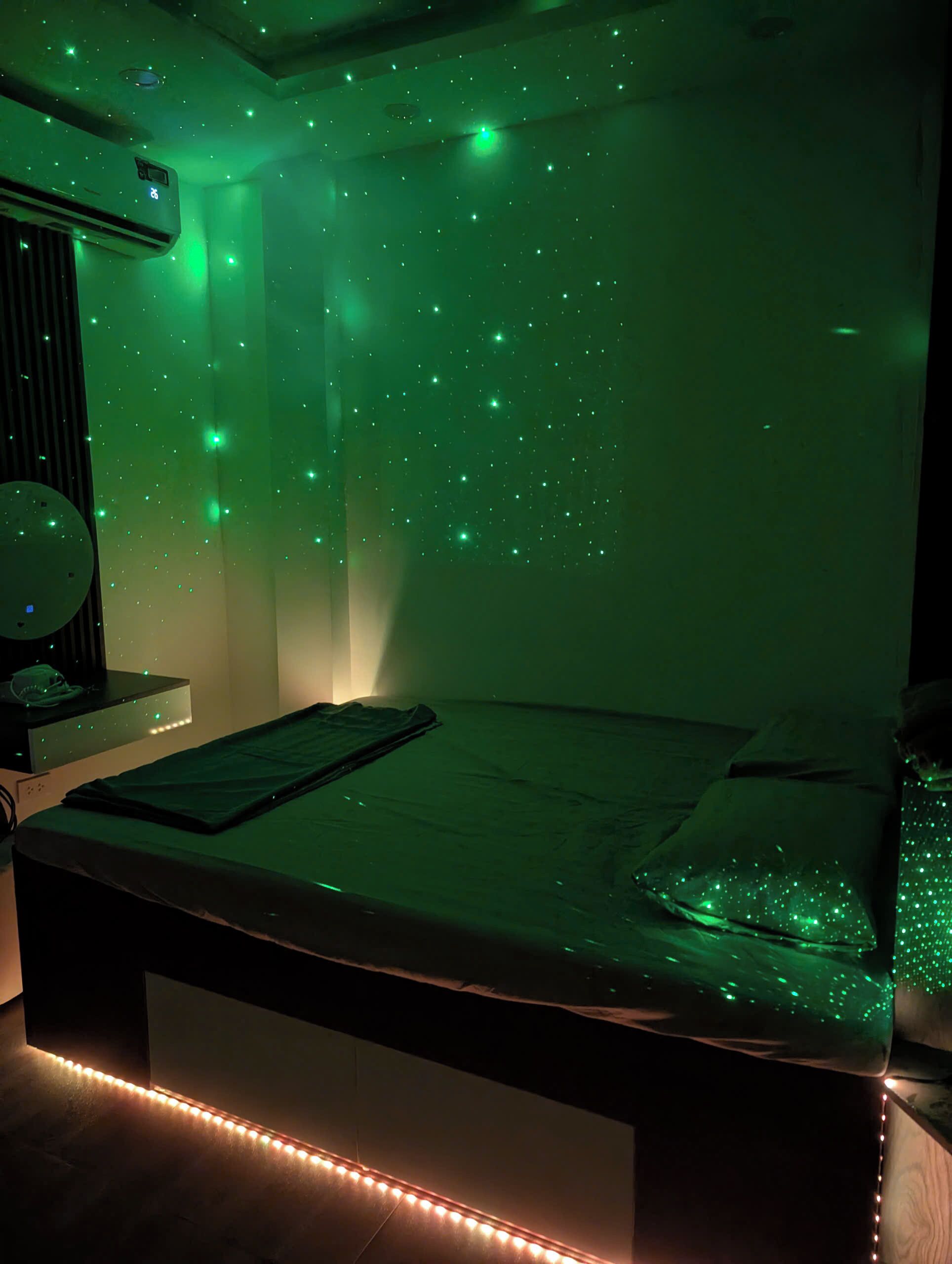 A room with a bed, a bedside table, and a wall with a starry light projection.
