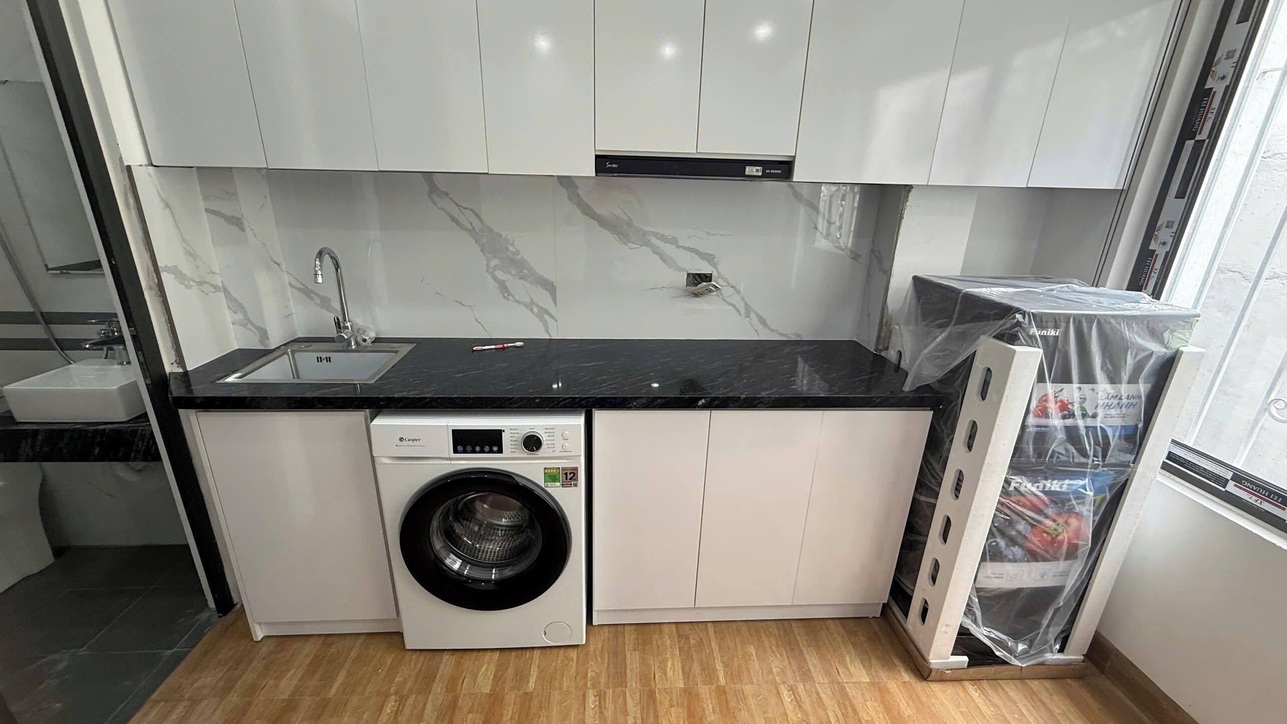 A compact kitchen with white cabinets, a black countertop, a built-in washing machine, and a sink.