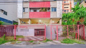 A building with a red and white facade, a gated entrance, and a staircase leading to the entrance. - Apto pet Friendly c Garagem em Rio Vermelho (Salvador)