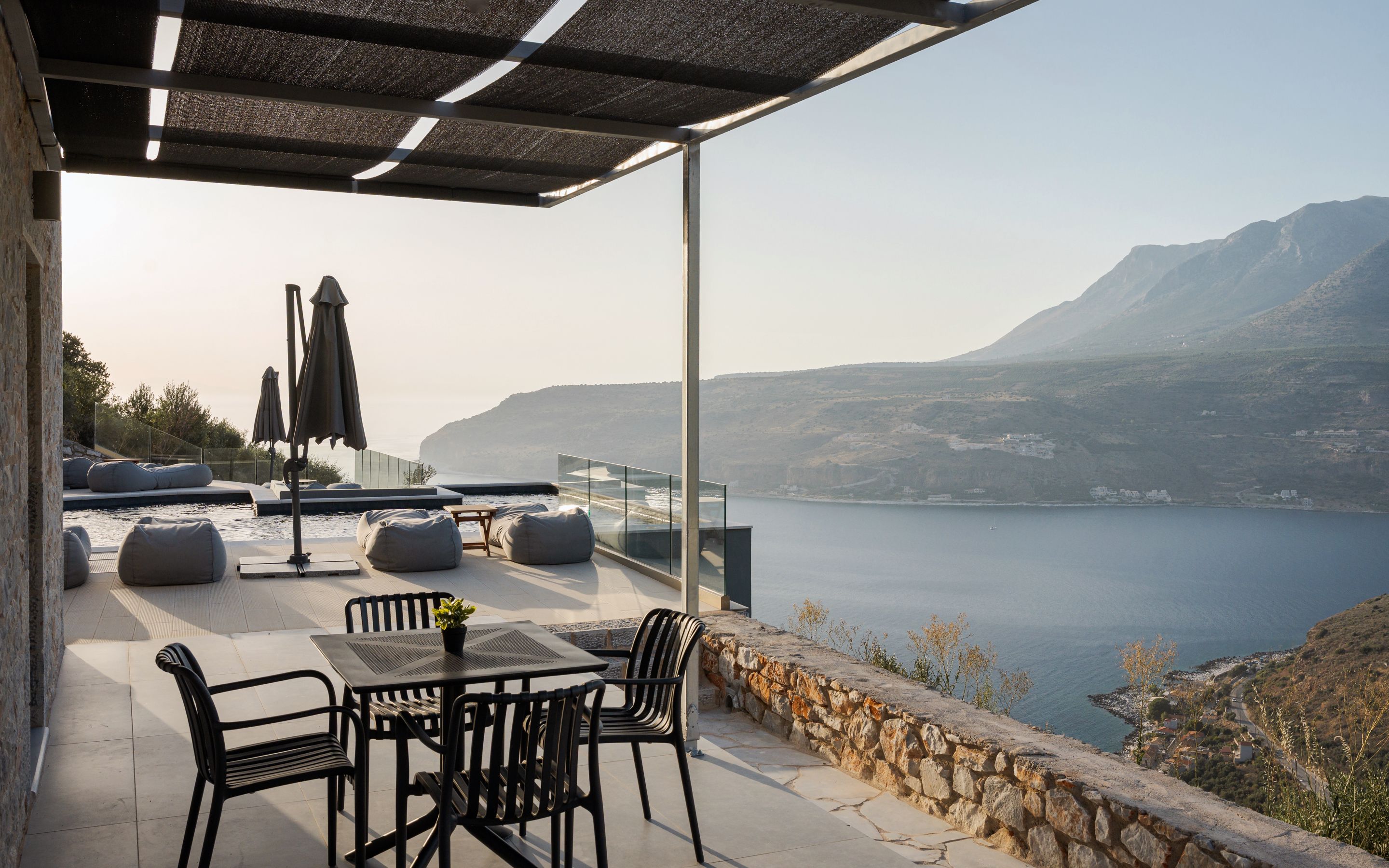 Ein Außenbereich mit Sitzgelegenheiten, Tisch, Stühlen, einem Pool und Blick auf Meer und Berge.