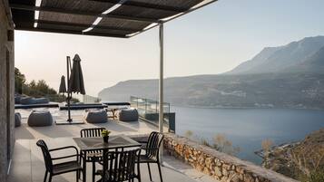 Ein Außenbereich mit Sitzgelegenheiten, Tisch, Stühlen, einem Pool und Blick auf Meer und Berge.