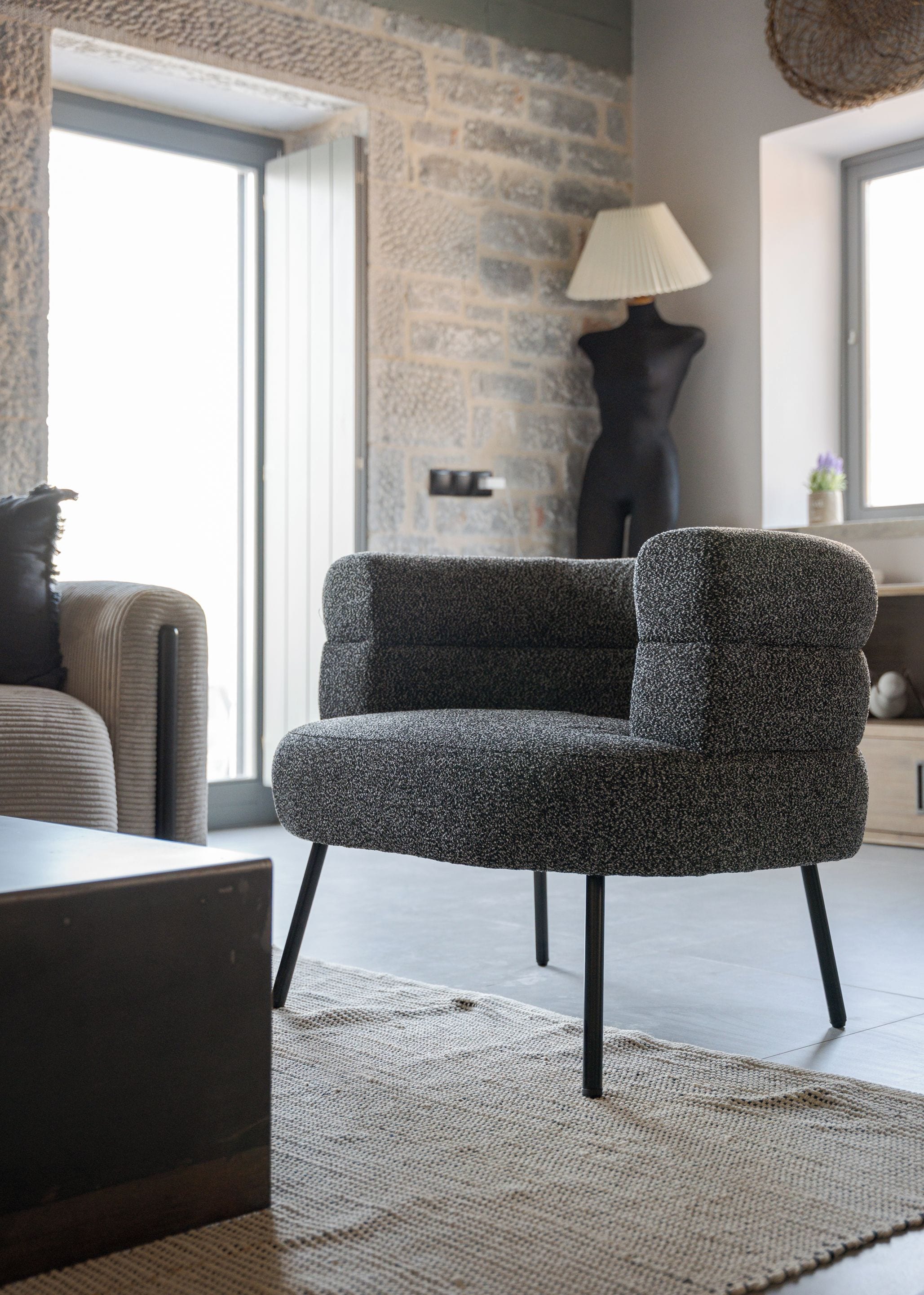 A modern living room with a textured armchair, a sofa, a lamp, and a stone wall.