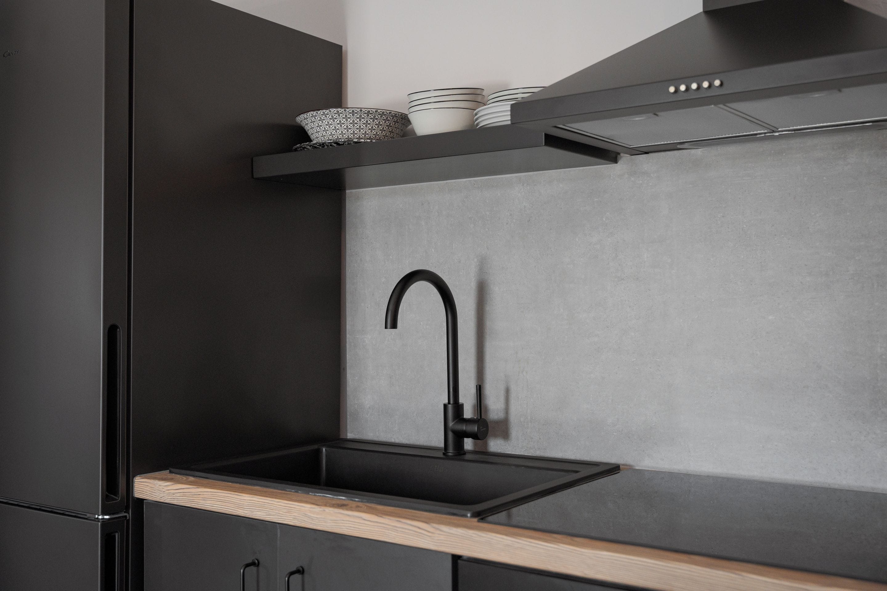 Een moderne keuken met een zwarte spoelbak, een houten aanrechtblad en zwarte kastjes.