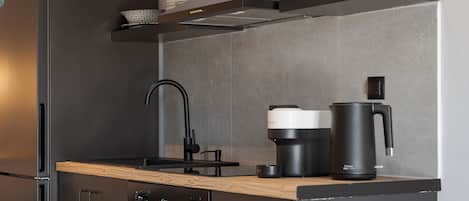 A modern kitchen with a stainless steel refrigerator, a built-in oven, a coffee maker, and a kettle on the countertop.