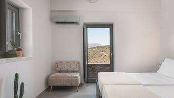 Un dormitorio con cama, ventana con vistas a un paisaje desértico, planta en maceta y unidad de aire acondicionado.