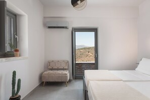 Un dormitorio con cama, ventana con vistas a un paisaje desértico, planta en maceta y unidad de aire acondicionado.