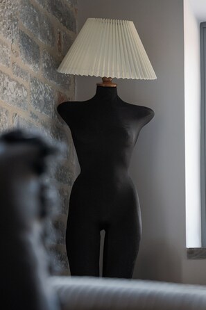 Un mannequin coiffé d’un abat-jour plissé, placé devant un mur de pierre.