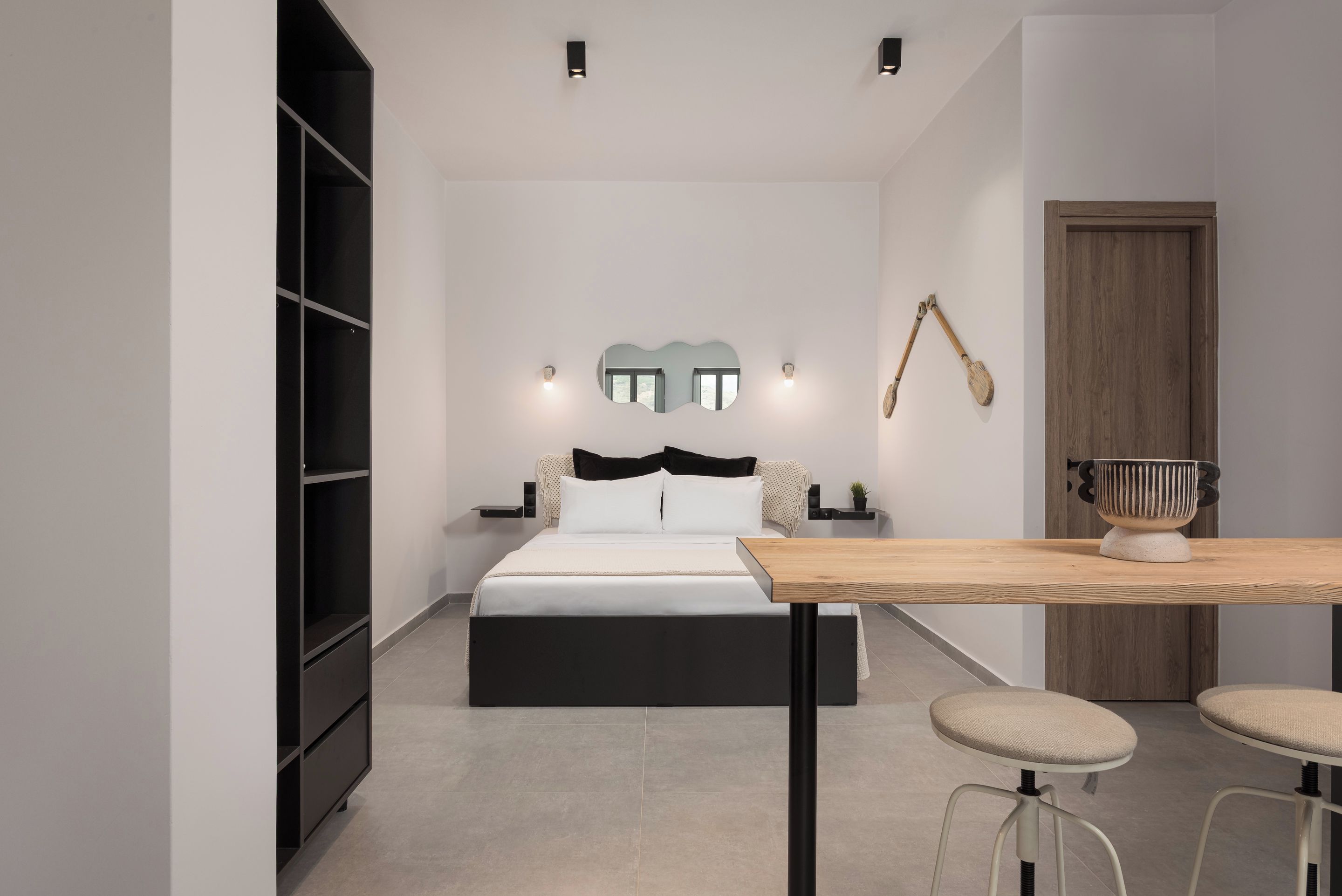 Un dormitorio moderno con una cama, una mesa de madera y dos taburetes.