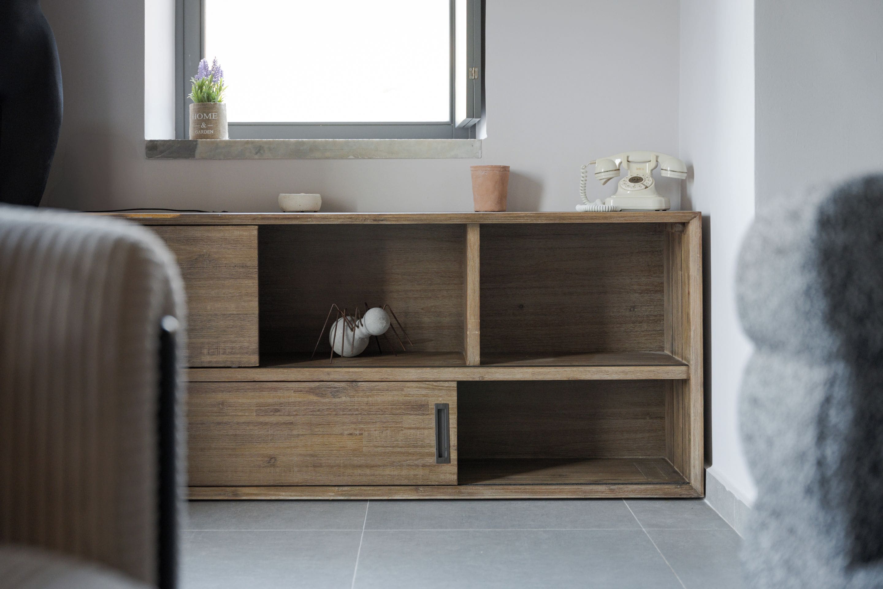 Una sala moderna con un mueble de madera, una pequeña planta en maceta y un teléfono antiguo.