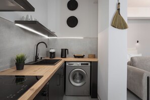 Una cocina compacta con lavadora integrada, un lavamanos y una cafetera.