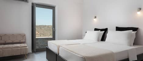 Une chambre moderne avec un grand lit, un canapé et une vue sur un paysage désertique, visible à travers une porte vitrée.