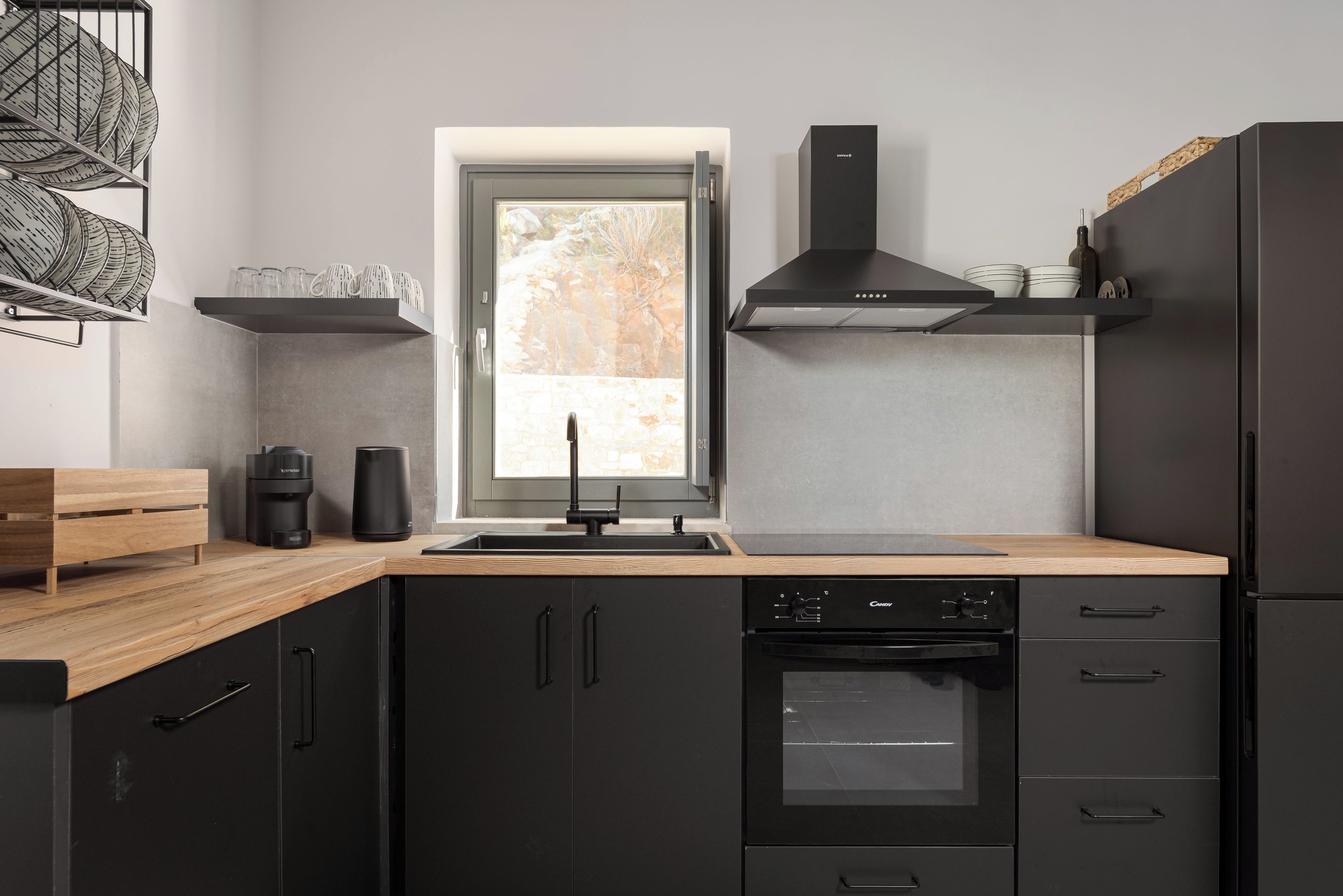 A modern kitchen with black cabinetry, a built-in oven, and a window with a view of the outdoors.