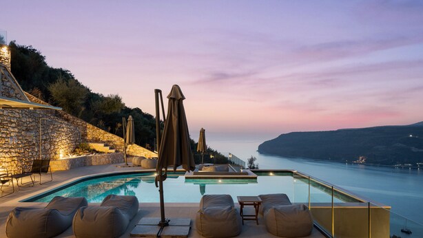 Zona de piscina con sillas de descanso y vista al mar al atardecer.