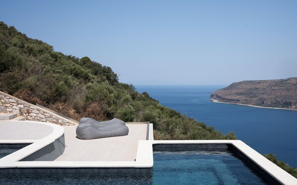 An infinity pool with a stone wall and a cushion, overlooking a coastal landscape. - The One Limeni (Areopoli)