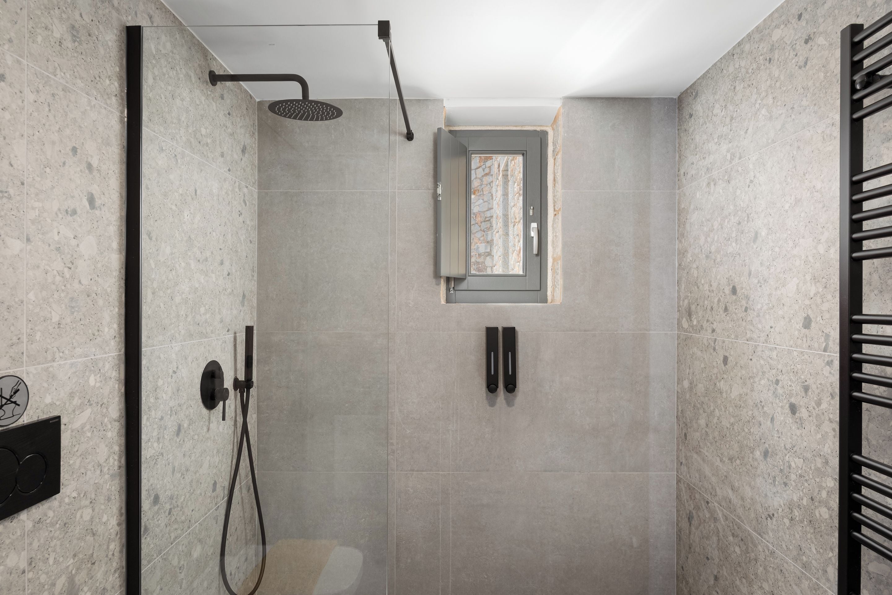 A modern shower with a glass door, a towel rack, and a wall-mounted control panel.