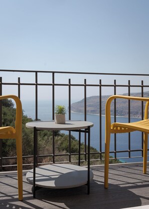Un balcón con una mesa redonda y dos sillas amarillas, con vistas al agua y colinas.