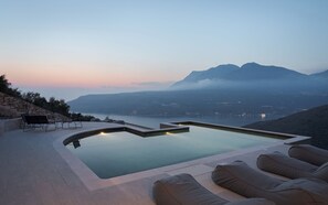 Una piscina con lettini e un muro in pietra, con vista su una valle e montagne.