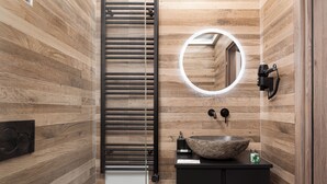 Un baño moderno con pared de madera, un perchero, un lavabo con cuenca de piedra y un espejo con luz circular.