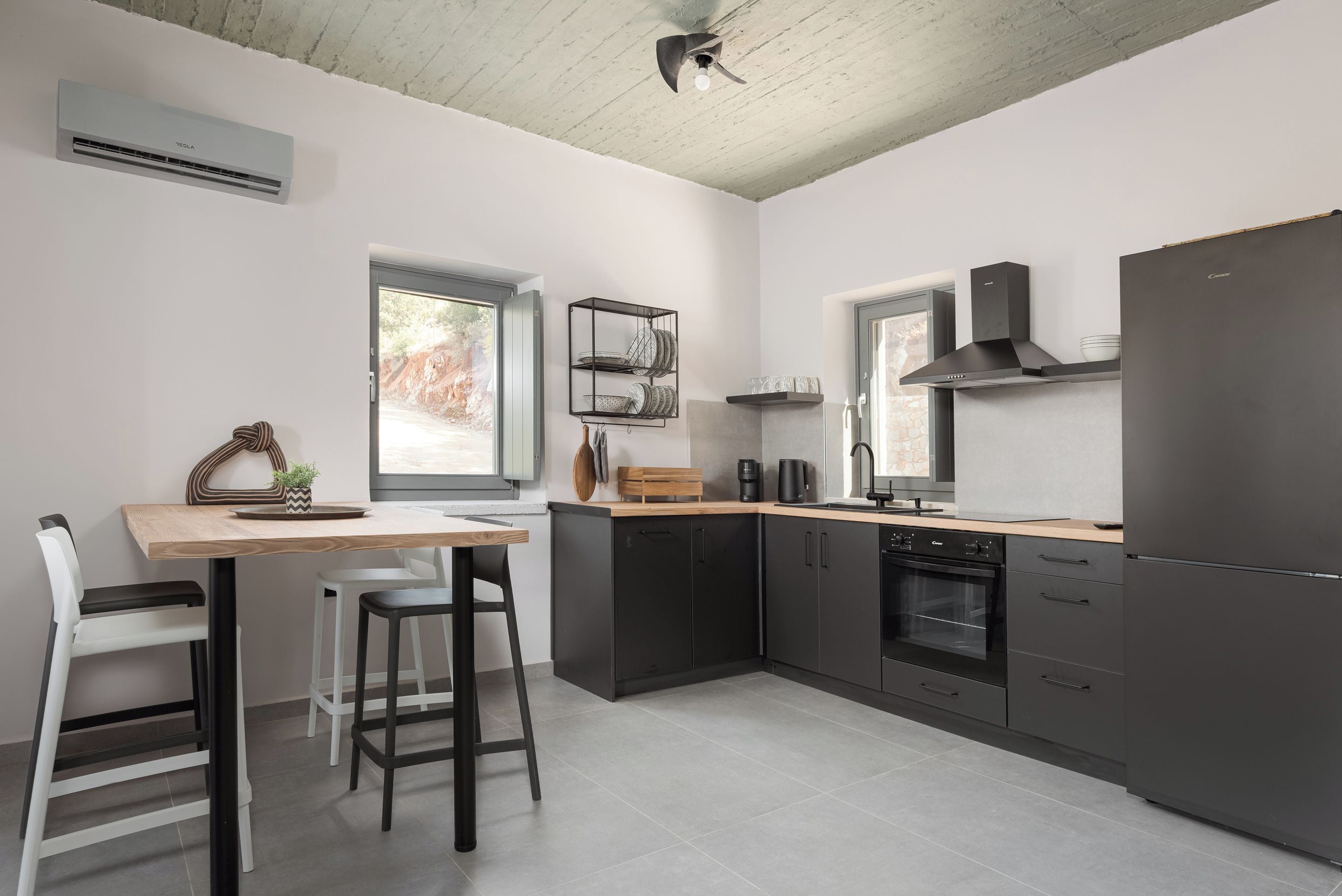 Una cocina moderna con una mesa de madera, taburetes de bar, horno empotrado y un refrigerador negro.