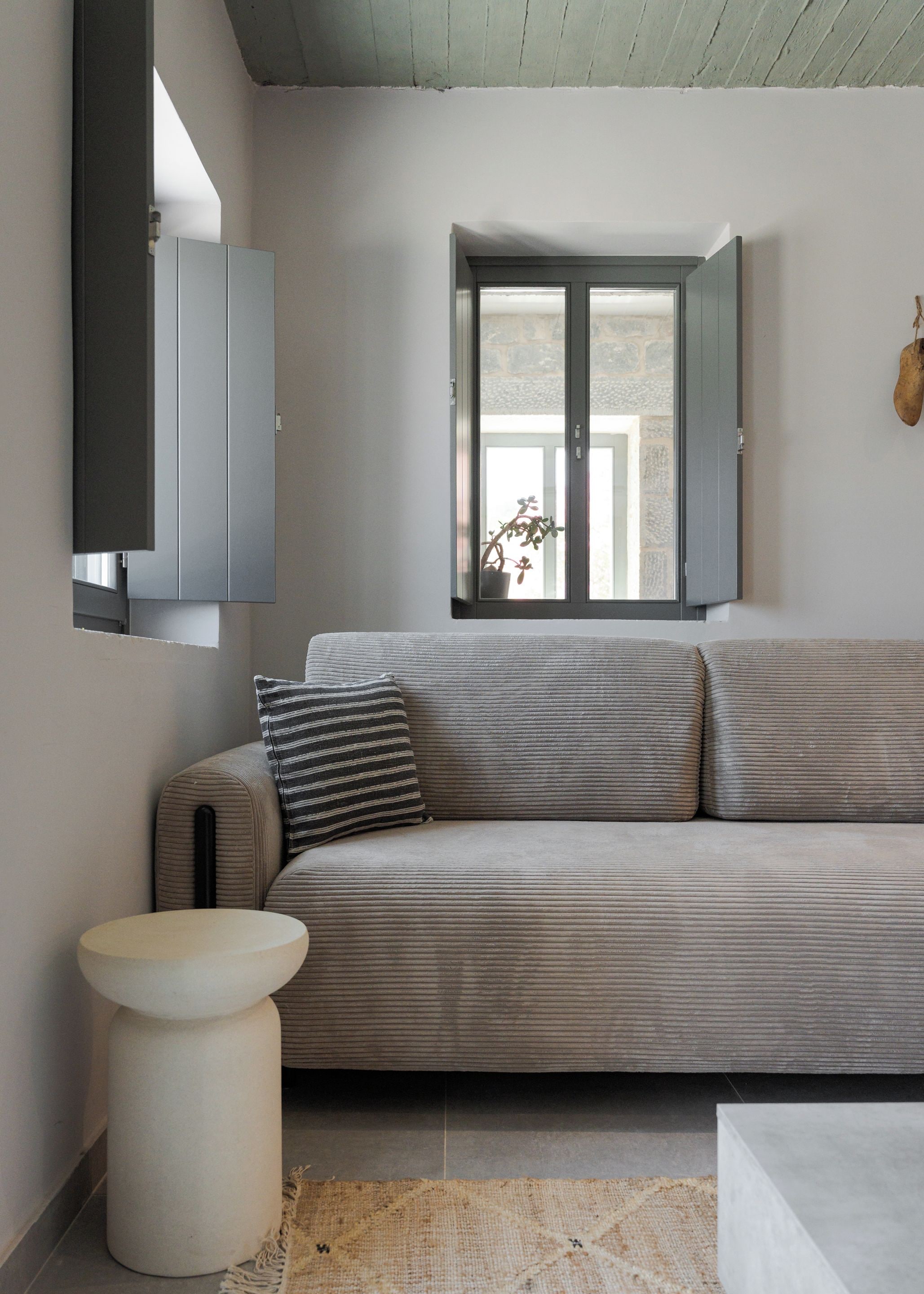 Una sala moderna con un sofá gris, una mesita redonda blanca y una ventana con vistas al exterior.