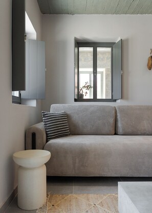 Een moderne woonkamer met een grijze bank, een rond wit bijzettafeltje en een raam met uitzicht op buiten.