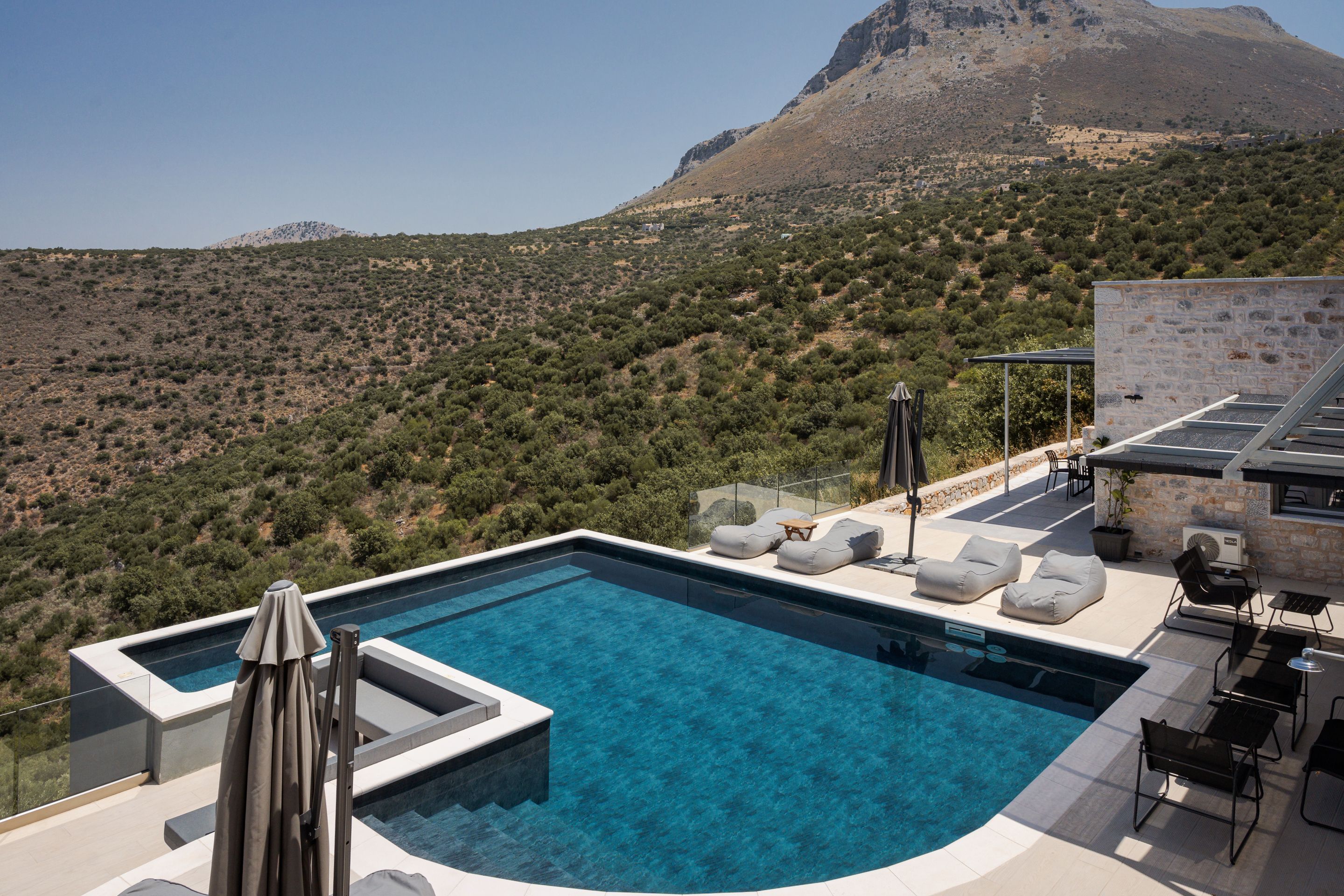 Piscina infinita en la azotea con sillas de descanso y una mesa, con vistas a un paisaje montañoso.