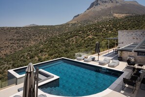 Piscina infinita en la azotea con sillas de descanso y una mesa, con vistas a un paisaje montañoso.
