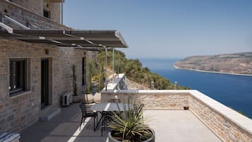 Un edificio de piedra con un patio, mobiliario exterior y vista al mar.