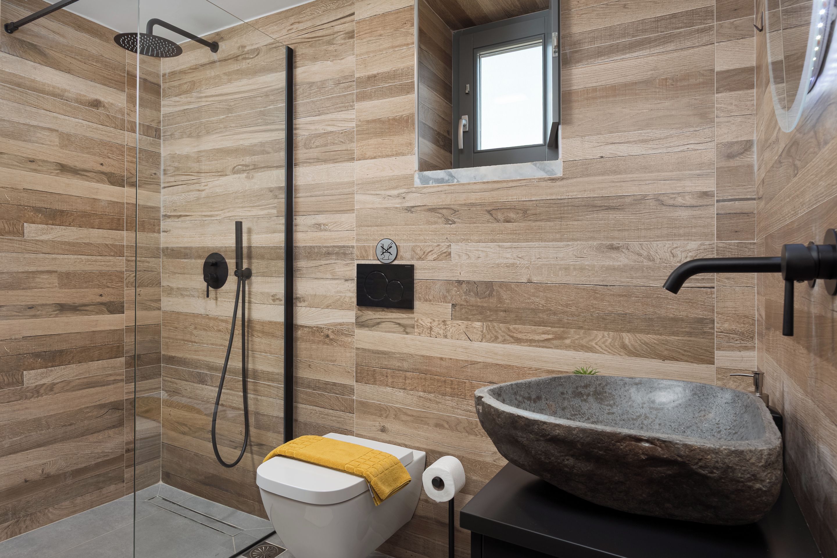 Un baño moderno con diseño de pared de madera, un lavamanos de piedra y una ducha con mampara de vidrio.