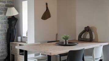 Un comedor con mesa de madera, sillas blancas y negras, una lámpara negra y una planta decorativa sobre la mesa.