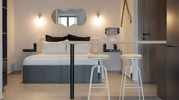A modern bedroom with a bed, two white bar stools, a small table, and a mirror on the wall.