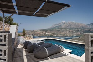 A pool area with a mountain view, outdoor seating, and a clear sky.