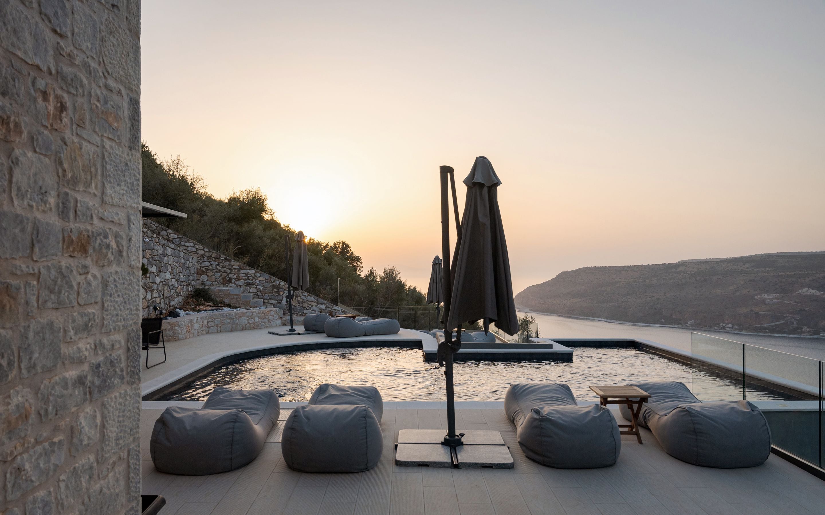 A poolside area with stone walls, seating, and a view of the water.