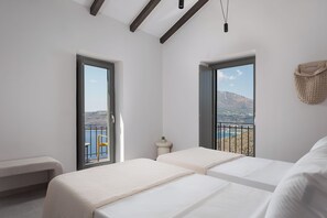 A bedroom with two beds, large windows, a balcony, and a view of a mountainous landscape. - The One Limeni (Areopoli)