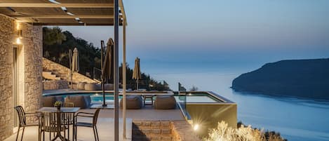 Zona junto a la piscina con mobiliario exterior, vistas al mar y un muro de piedra.