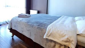 Ein modernes Schlafzimmer mit einem großen Bett, Holzboden, einem dunklen Kopfteil und Blick ins Freie.