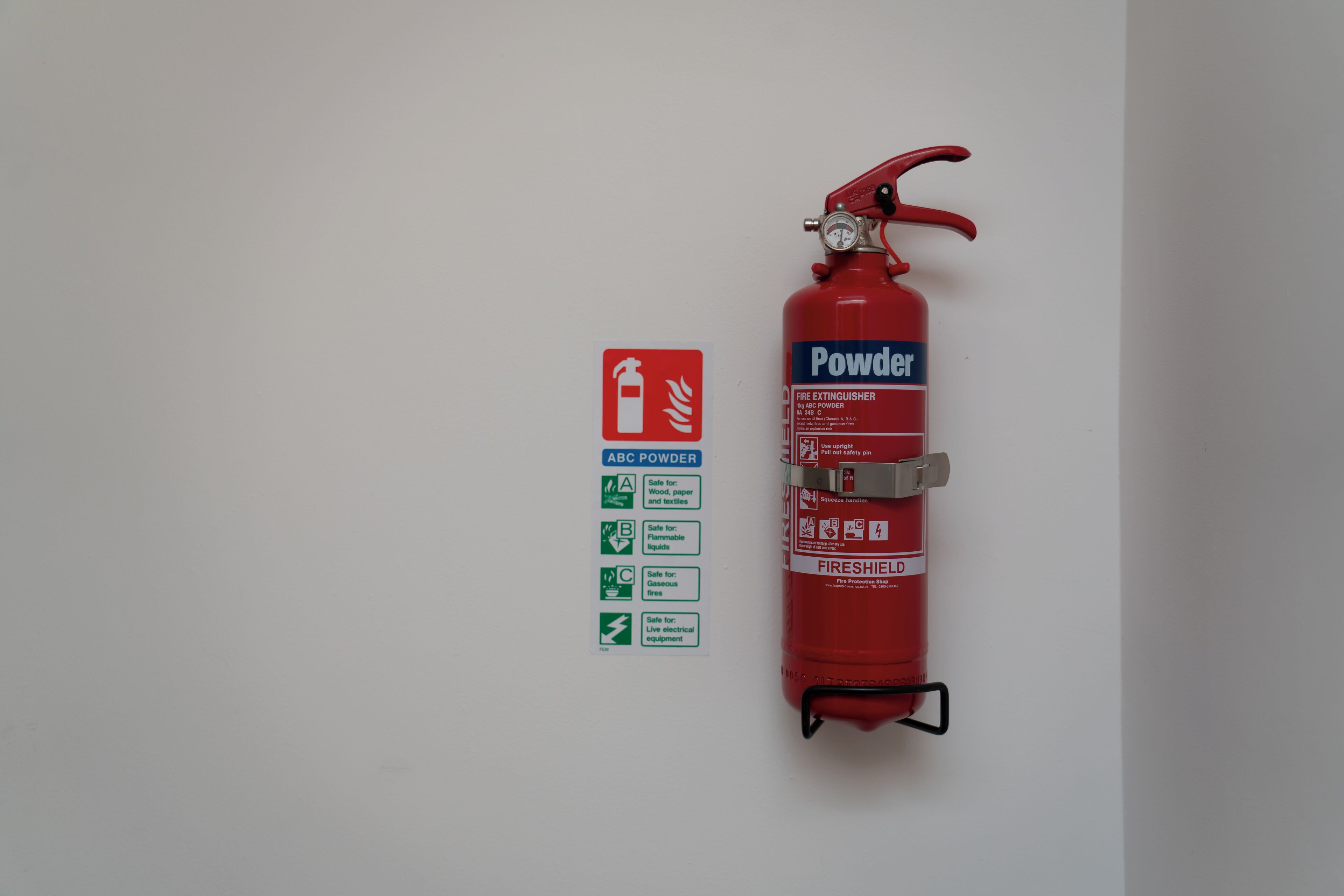 Estintore rosso montato su una parete bianca accanto a un cartello di sicurezza antincendio.