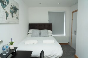 Una camera da letto ordinata con un letto grande, un comodino con bottigliette d'acqua, una mappa del mondo appesa al muro e una finestra con tende.
