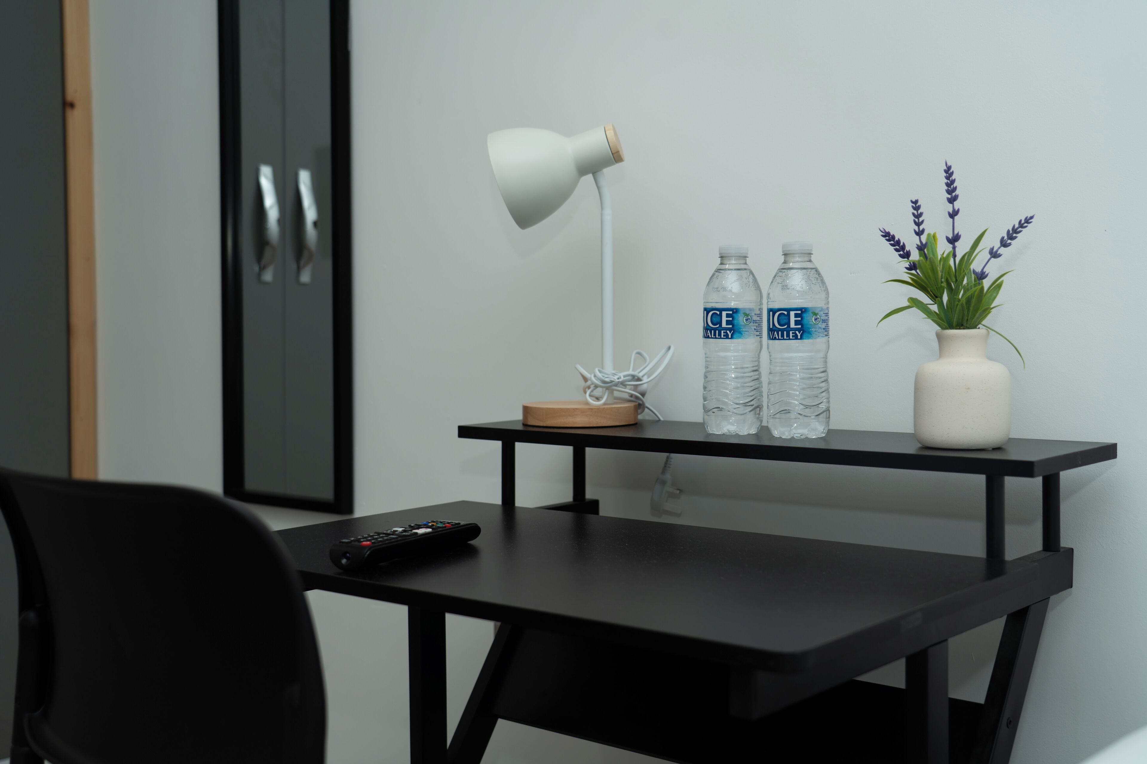 Ein modernes Zimmer mit einem schwarzen Schreibtisch, einer weißen Lampe, zwei Wasserflaschen, einer kleinen Pflanze und einer Fernbedienung.
